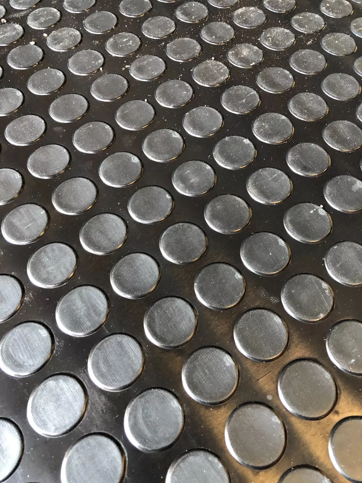 Close-up of a black metal surface with evenly spaced raised circular bumps (anti-slip tread).