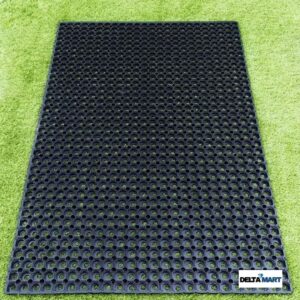 Black perforated rubber mat with circular holes laid on green artificial turf; DeltaMart logo in the corner.