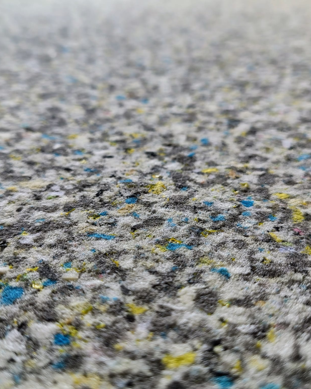 Close-up of a textured carpet with gray base and scattered blue, yellow, and white flecks.