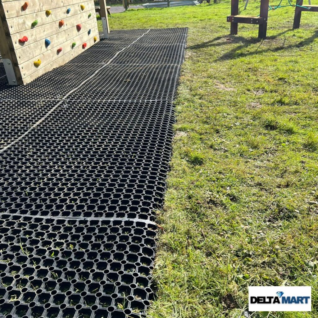 Black rubber grass mats for a playground laid beside a wooden climbing wall on the lawn